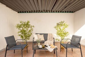 Een terras met een tafel gedekt voor twee personen, twee stoelen, een bankje en twee potten met bamboeplanten.