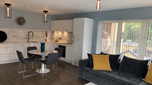 Una cucina moderna con mobili bianchi, una zona pranzo con un tavolo rotondo e sedie, e un divano grigio con cuscini gialli.