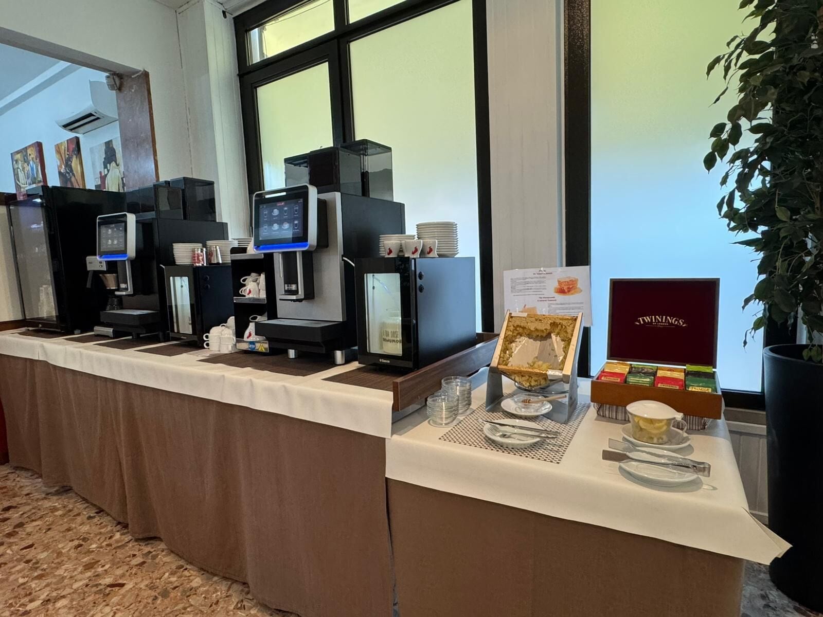 Un buffet avec des machines à café, une sélection de thés Twinings et une plante.