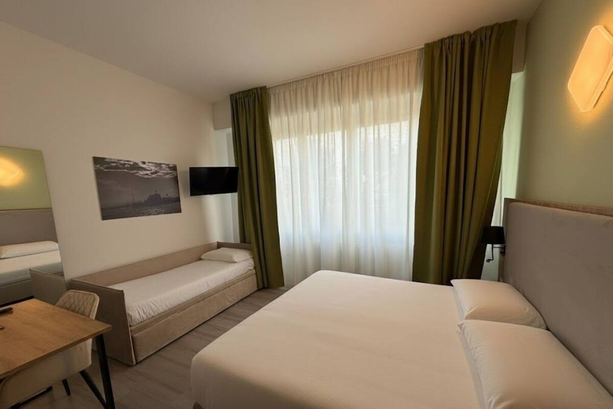 A hotel room with a bed, a sofa bed, a desk, and a TV.