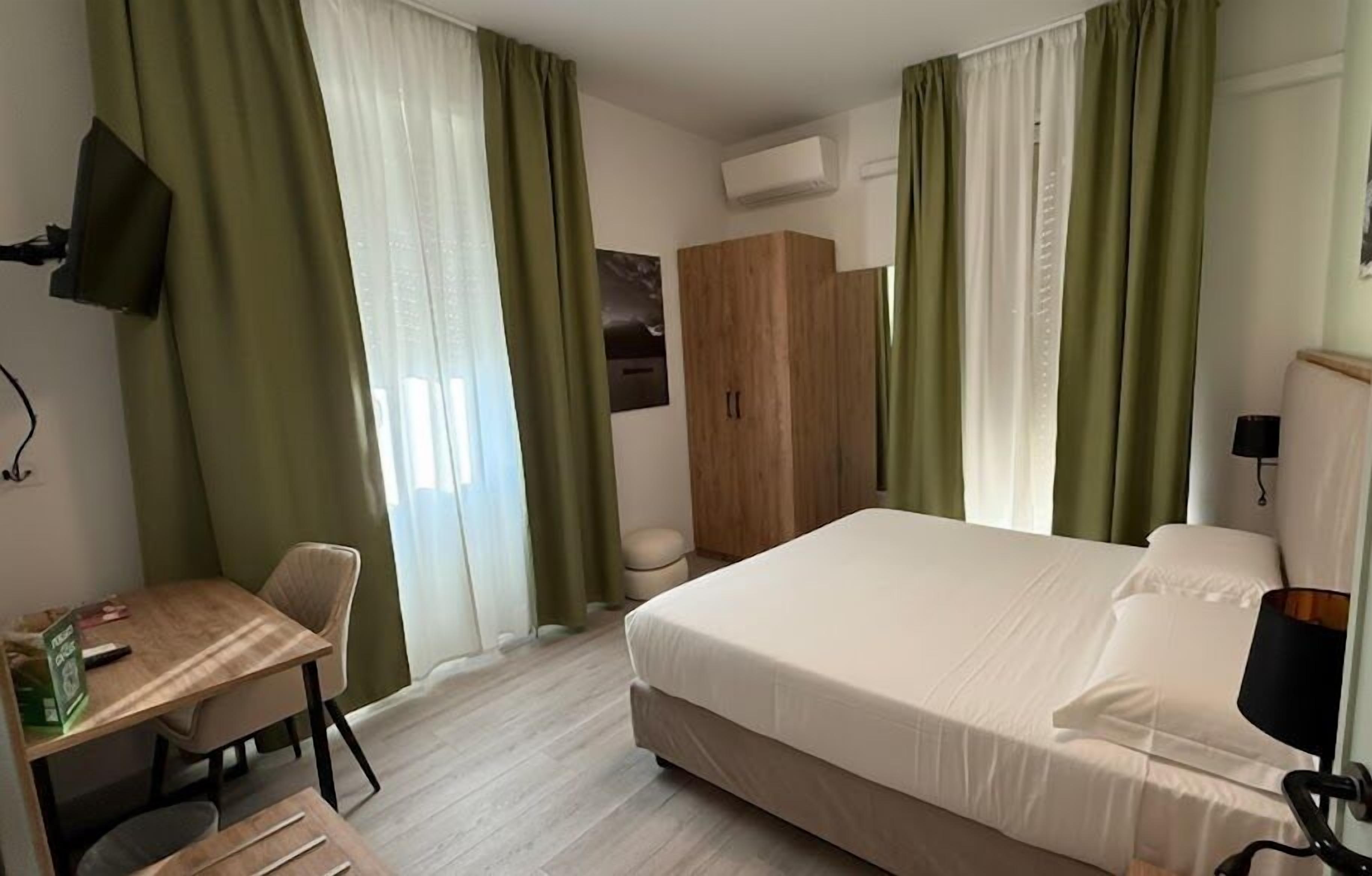 Ein Hotelzimmer mit Bett, Schreibtisch, Stuhl, Kleiderschrank und Fernseher.