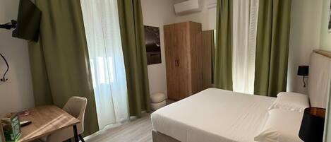 Ein Hotelzimmer mit Bett, Schreibtisch, Stuhl, Kleiderschrank und Fernseher.