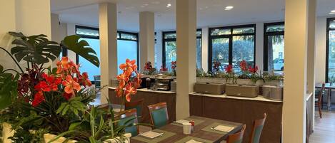 Un espace de restauration moderne, doté de hauts plafonds, de grandes fenêtres et de plantes d’intérieur.