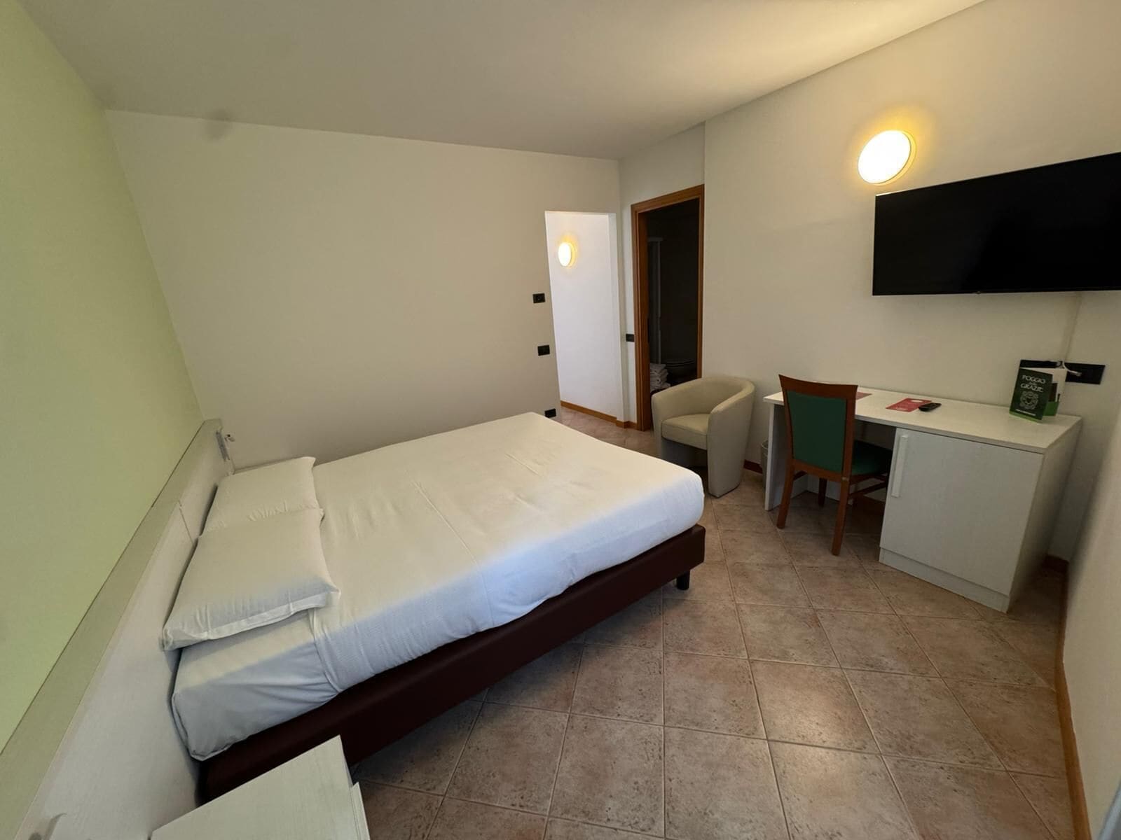 Hotellihuone, jossa on yksi sänky, työpöytä, tuoli ja seinälle asennettu televisio.