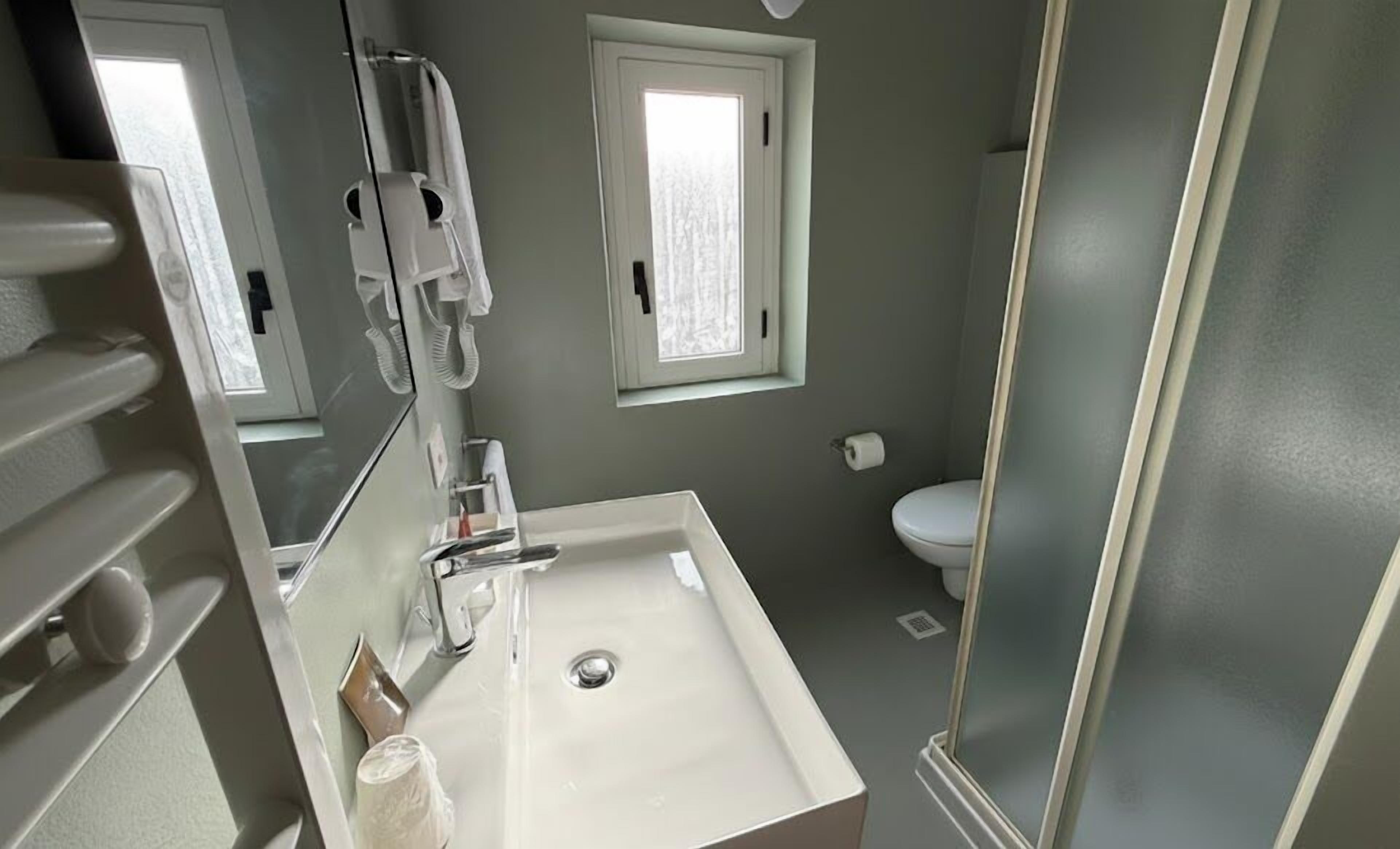 Ein Badezimmer mit einem weißen Waschbecken, einem Spiegel, einem Handtuchspender, einer Toilette und einem Fenster.