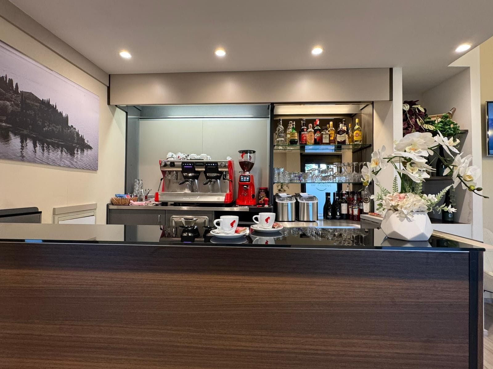 Zona de bar moderna con una máquina de café, una selección de botellas de licor y un jarrón de flores.