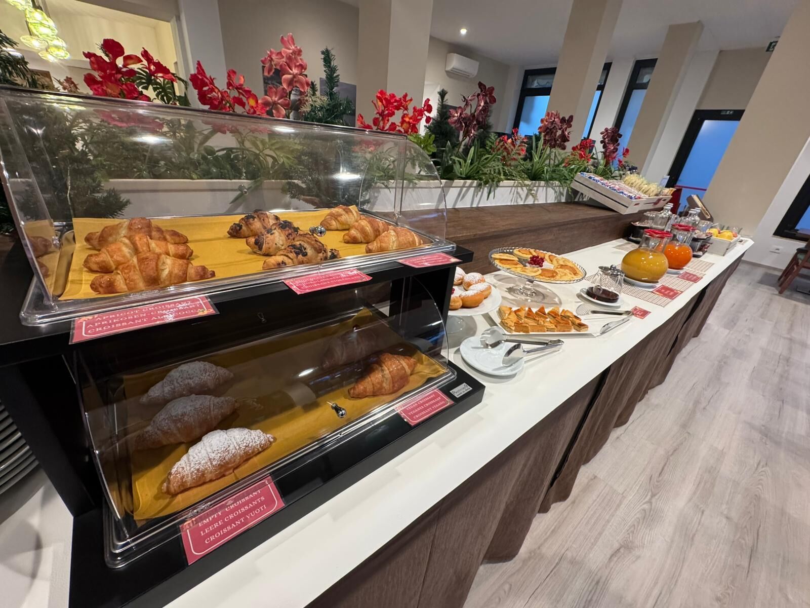 A buffet with various pastries and desserts, including croissants and muffins, displayed in glass cases.