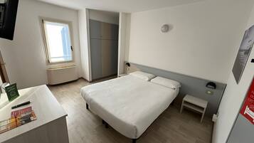 Habitación de hotel con cama, mesitas de noche, escritorio con silla, ventana, armario y televisión.