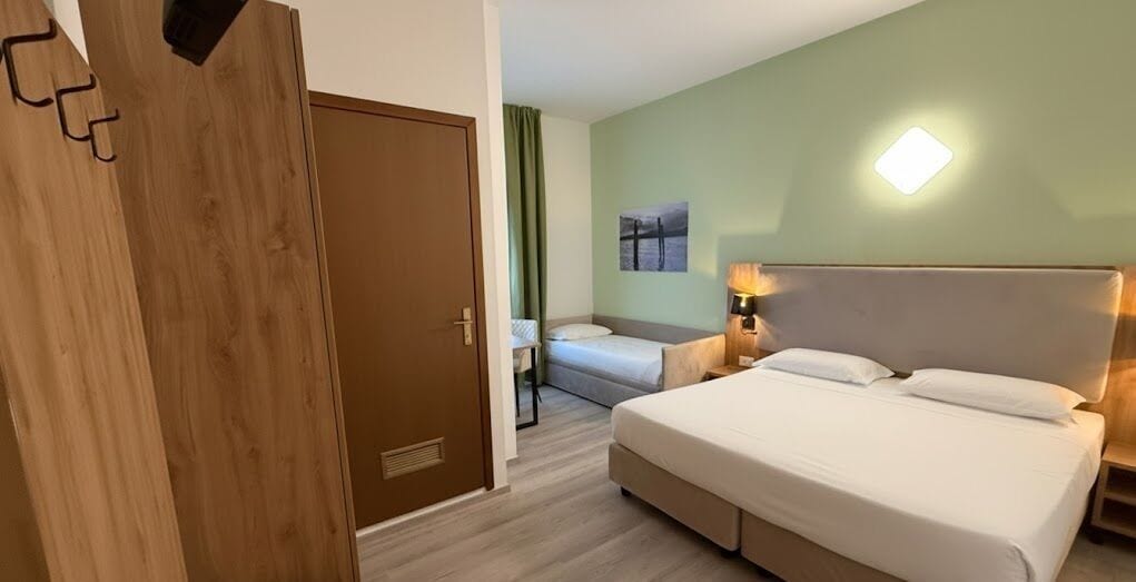 Une chambre d’hôtel avec un grand lit, un lit plus petit, une armoire et une table de chevet avec une lampe.
