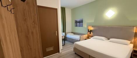Una camera d'albergo con un letto grande, un letto più piccolo, un armadio e un comodino con una lampada.