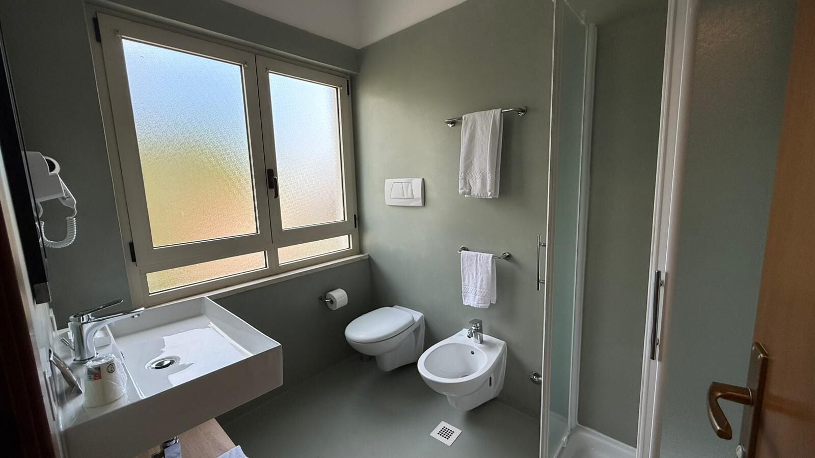 A bathroom with a window, a sink, a toilet, and a bidet.