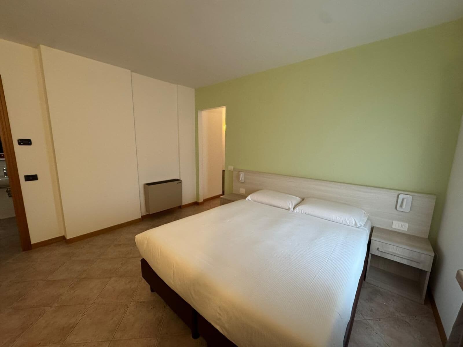 A bedroom with a large bed, a bedside table, a wardrobe, and a radiator.