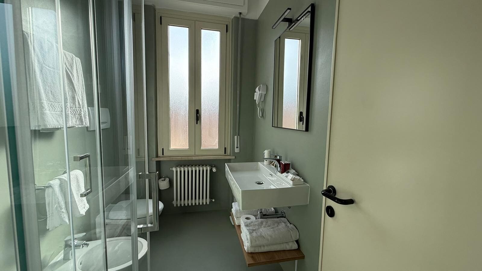 Un bagno con cabina doccia in vetro, un lavandino bianco con specchio e un termosifone.