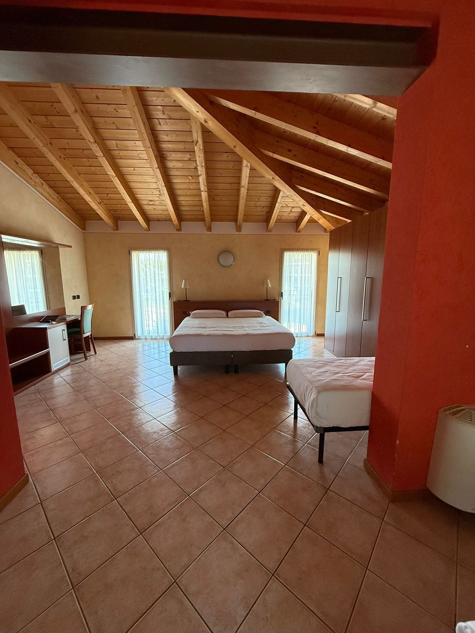 Una habitación amplia con techo alto, una cama grande, un escritorio y un armario.