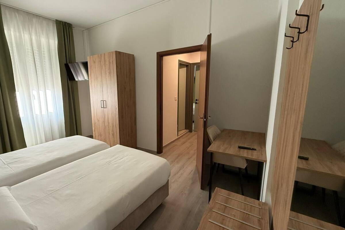 A hotel room with two beds, a desk, a wardrobe, and a TV.