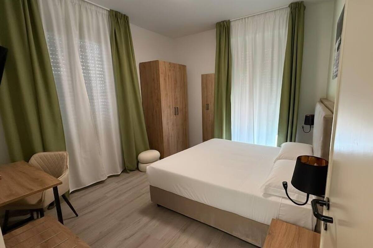 A hotel room with a bed, a desk, a chair, and a wardrobe.