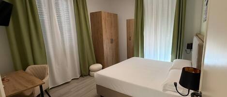 A hotel room with a bed, a desk, a chair, and a wardrobe.