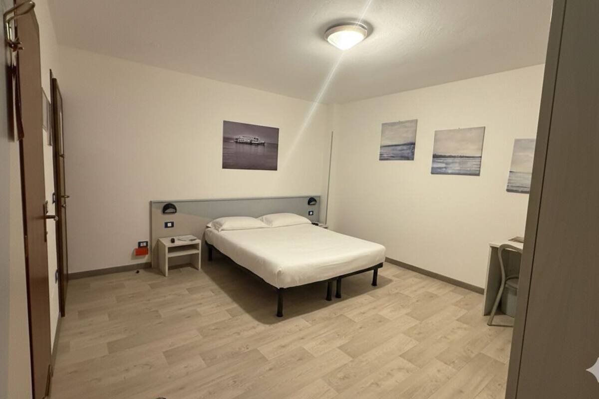A bedroom with a bed, a nightstand, a wall-mounted lamp, and a ceiling light.