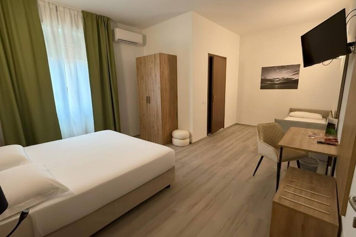 A hotel room with a bed, a desk, a chair, a television, and a wardrobe.