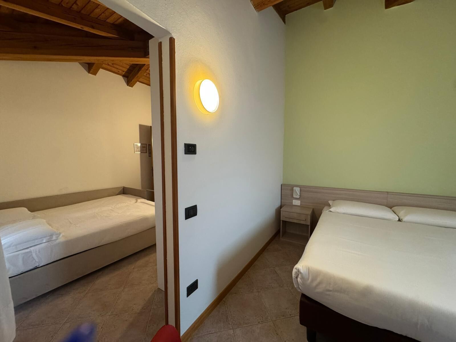 Quarto de hotel com duas camas, teto de madeira e luminária fixada na parede.