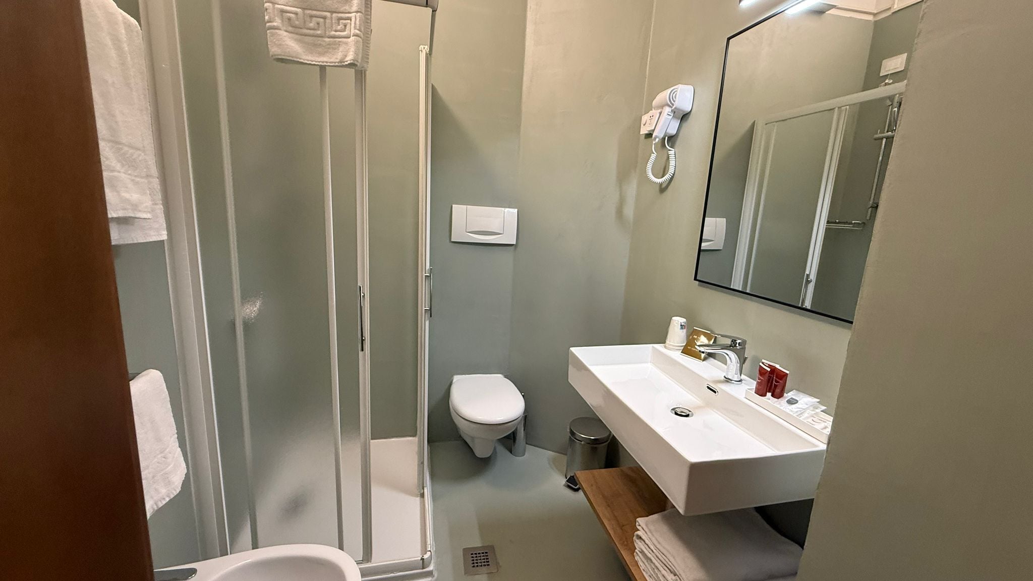 A bathroom with a glass-enclosed shower, a toilet, and a sink with a mirror above.