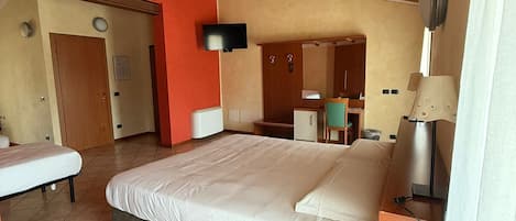 A bedroom with a large bed, a desk, a chair, a TV, and a bathroom visible in the background.