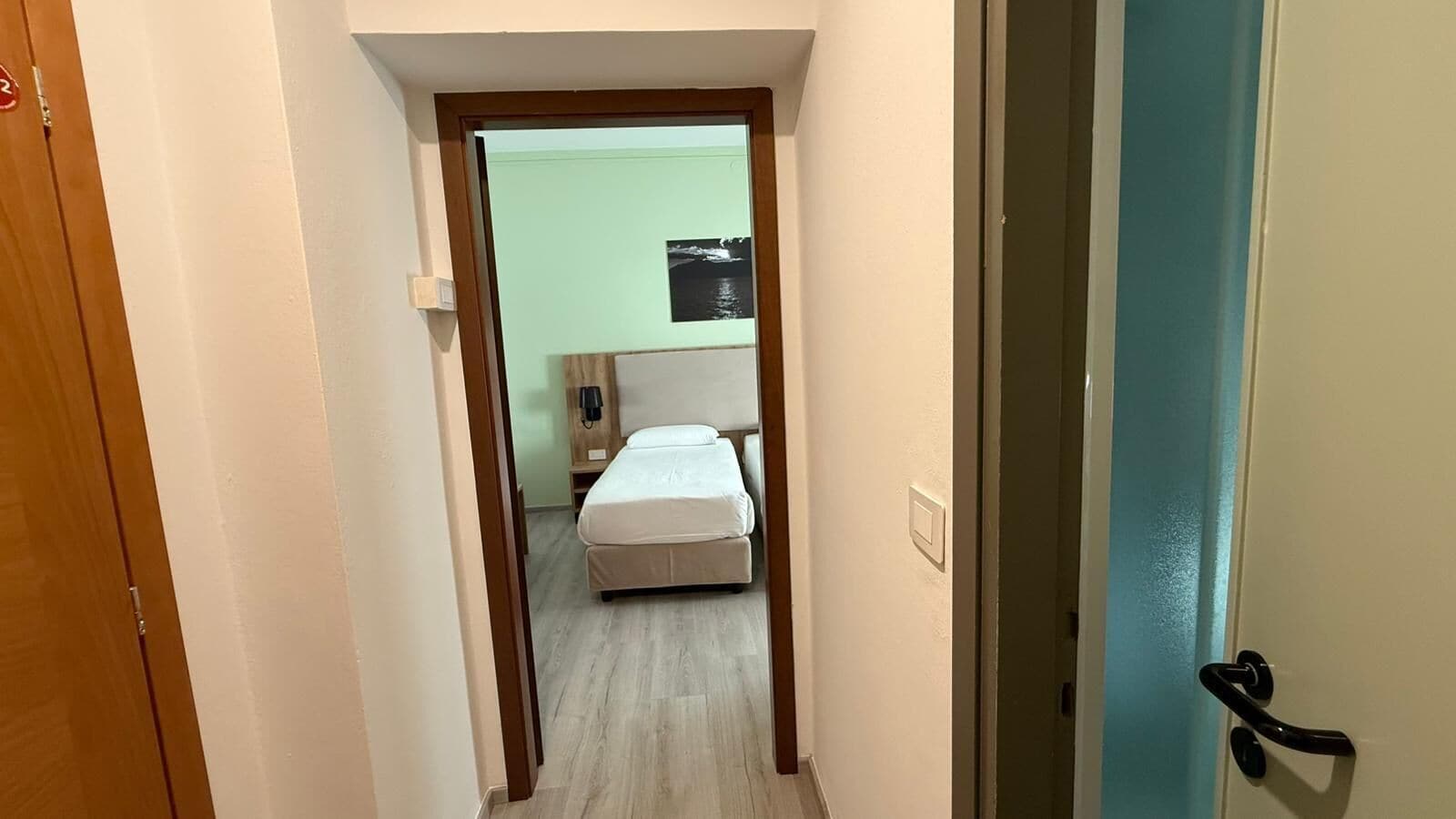 Un couloir étroit mène à une chambre qui contient un lit, une table de chevet et un téléphone fixé au mur.