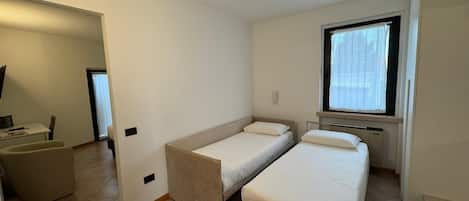 Quarto pequeno e limpo com duas camas de solteiro, uma mesinha e uma cadeira.