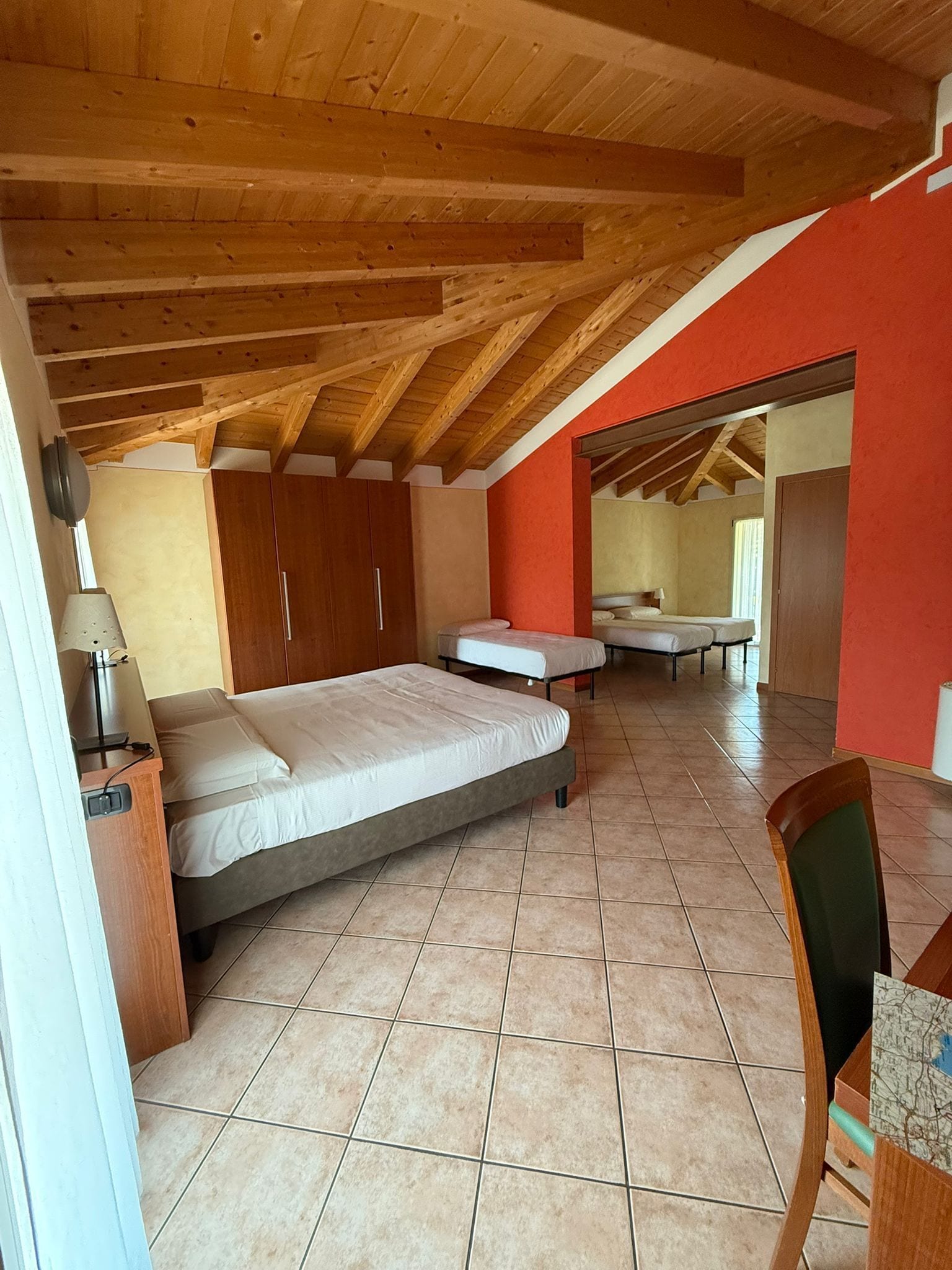 A bedroom with a large bed, a smaller bed, wooden ceiling beams, and a red wall.