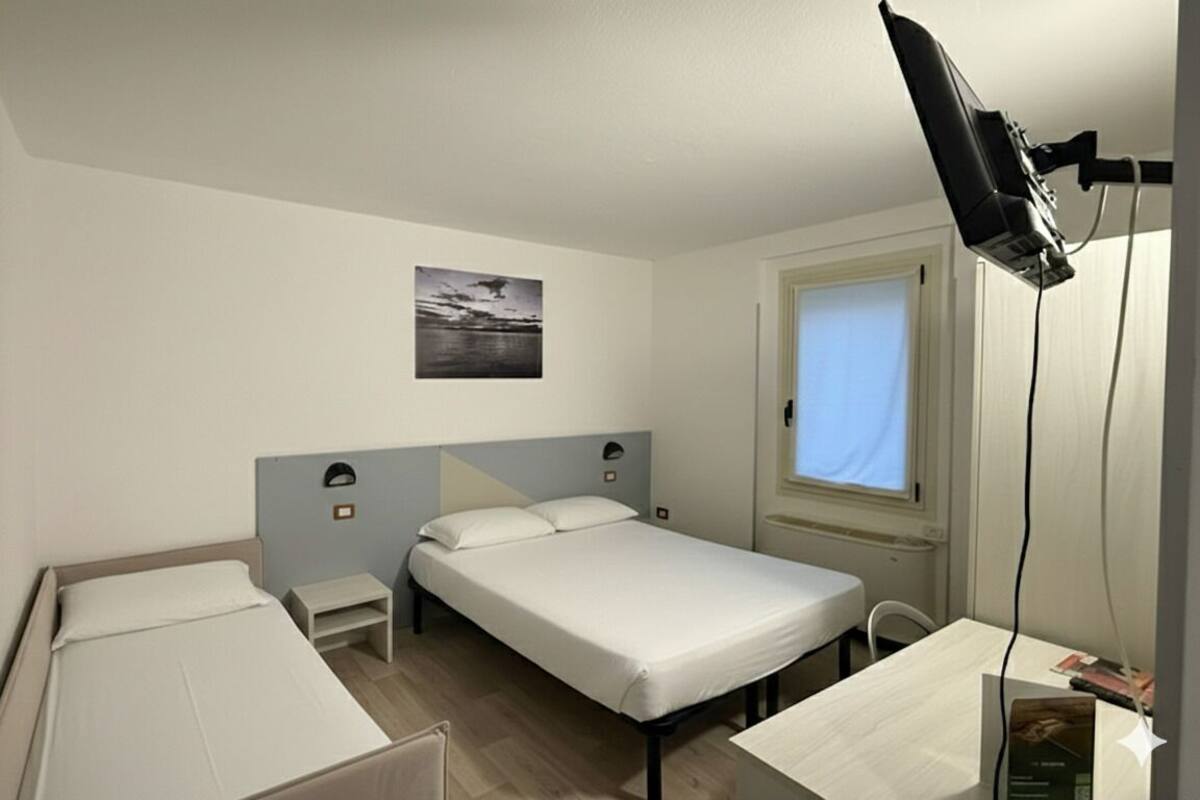 A small, clean room with two single beds, a desk, and a window.