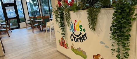 Un coin pour enfants avec une fresque murale, des plantes d’intérieur et des chaises en bois.