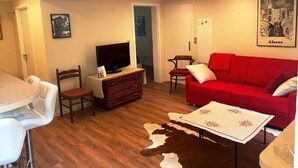 A living room with a red sofa, a television on a wooden cabinet, a dining table with chairs, and a cowhide rug. - Nice flat in villa, quiet 10mn from the center, streetcar 100m, free parking. (strasbourg)