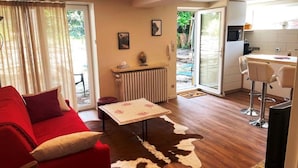 A living room with a red sofa, a coffee table, and a cowhide rug. There is a kitchen area with a microwave and a bar stool. - Nice flat in villa, quiet 10mn from the center, streetcar 100m, free parking. (strasbourg)
