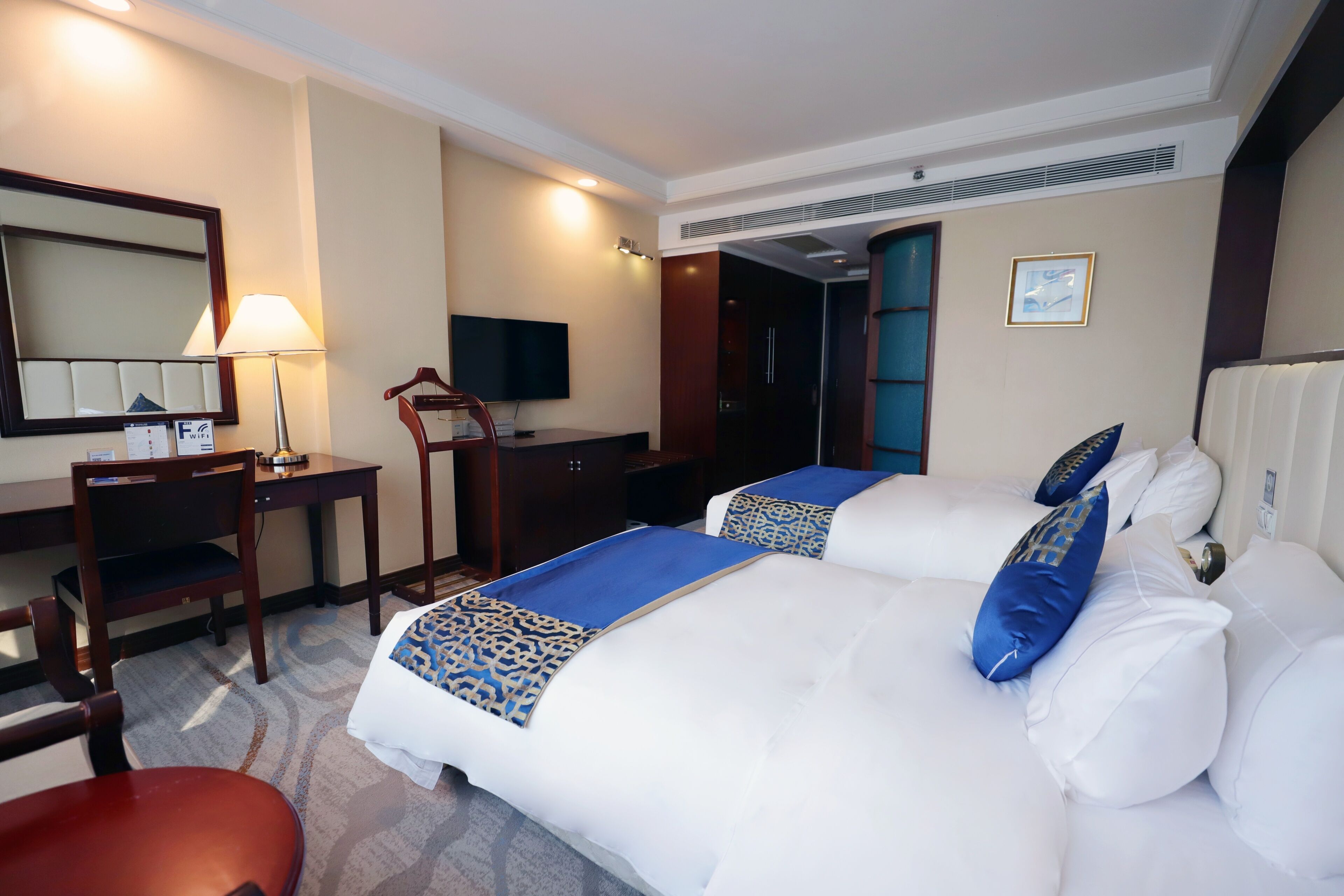 A hotel room with two beds, a desk, a chair, a TV, and a mirror.