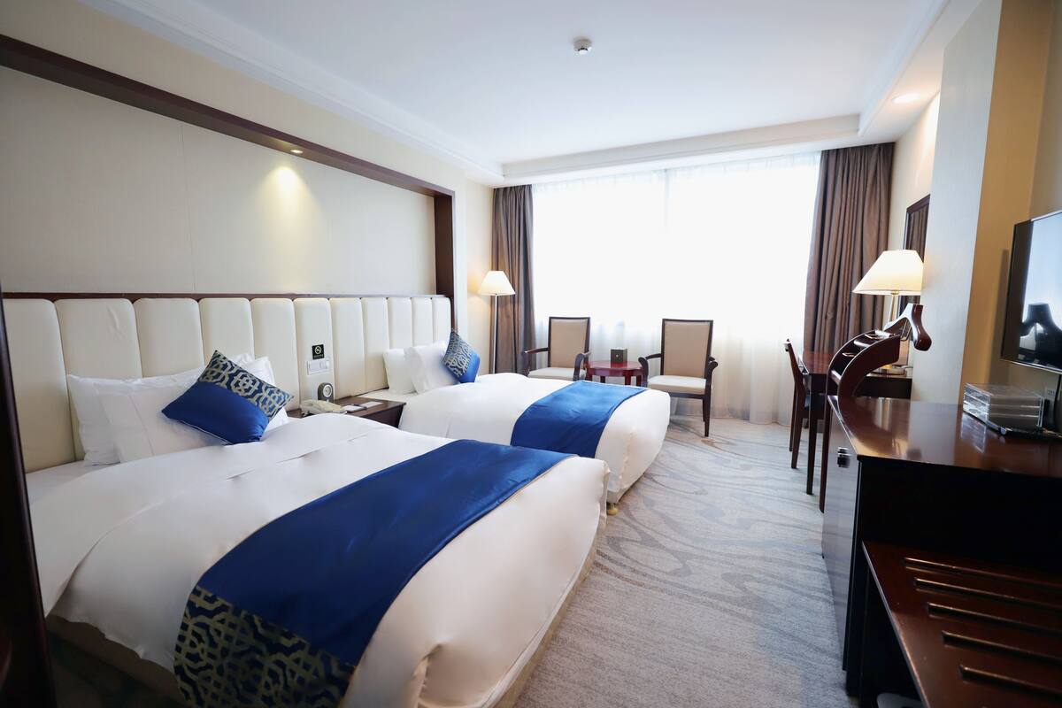 Une chambre d’hôtel avec deux lits, un bureau, des chaises, une télévision et une grande fenêtre.