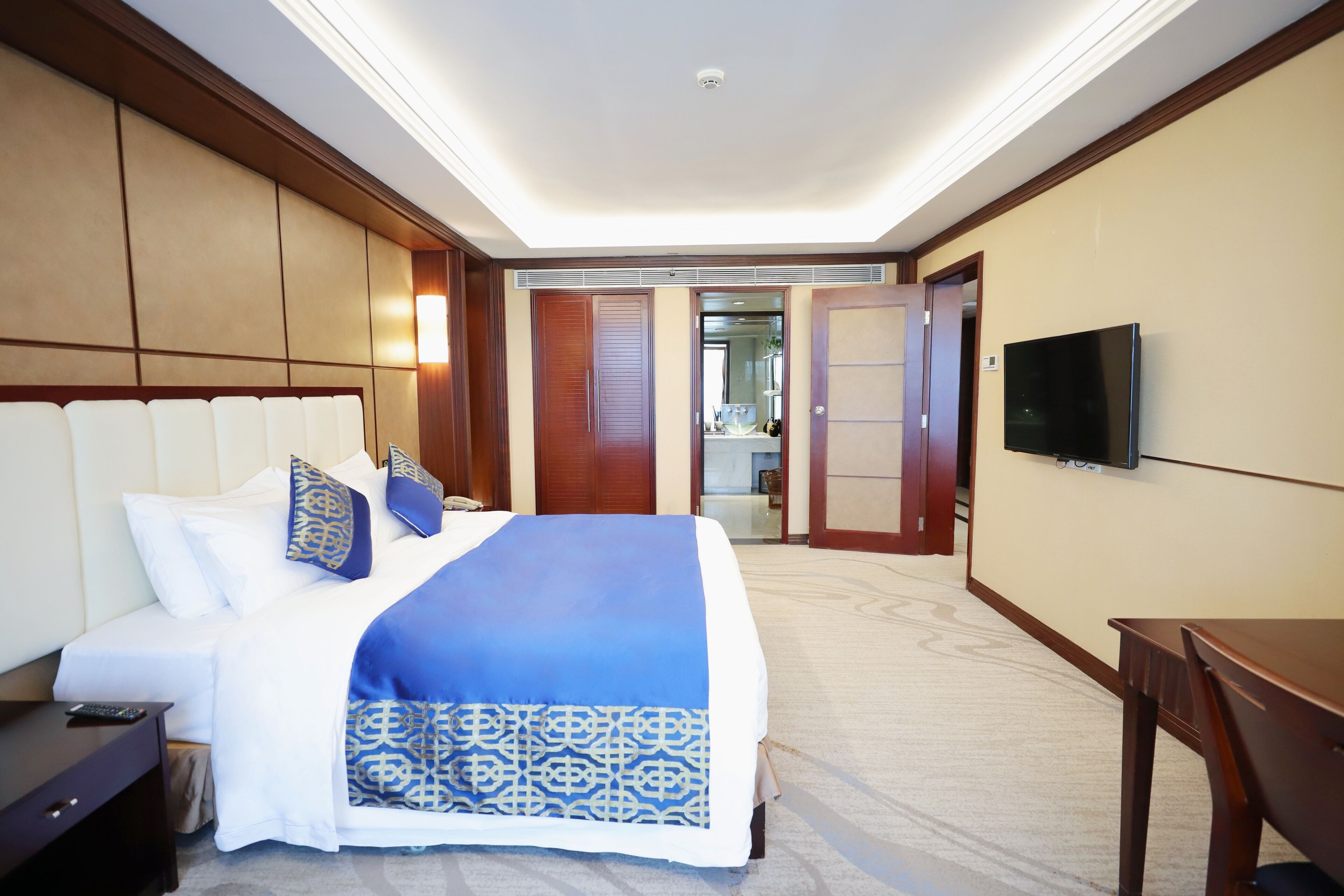 Habitación de hotel con una cama grande, un televisor montado en la pared y una mesita de noche de madera.