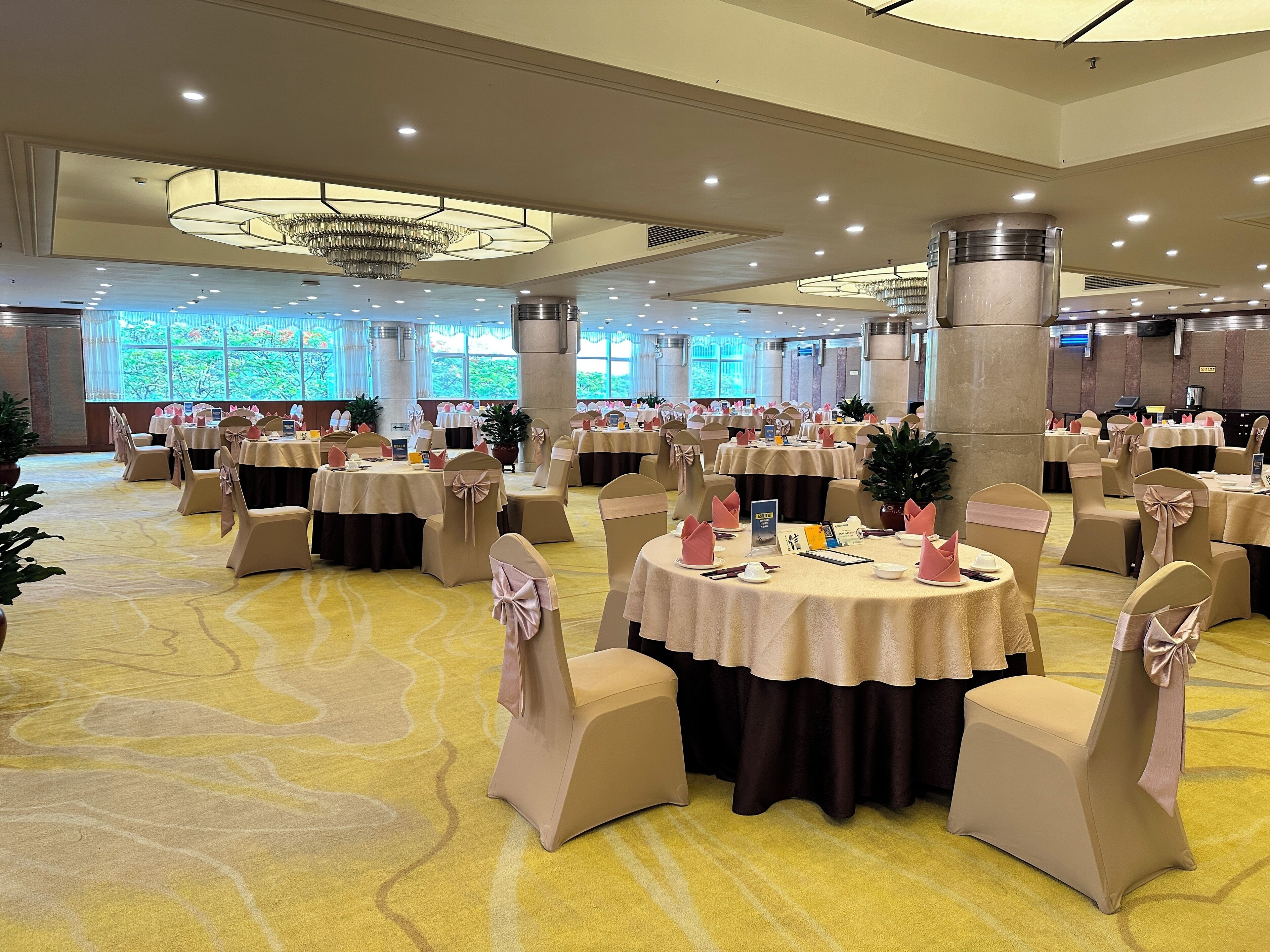 A banquet hall with round tables, beige chairs, and a yellow carpet.
