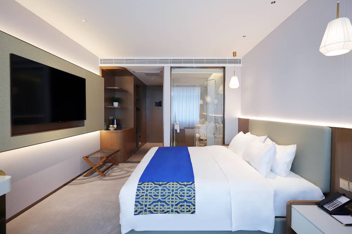 Une chambre d’hôtel moderne dotée d’un grand lit, d’un téléviseur à écran plat, d’un bureau avec une lampe et d’un dressing.
