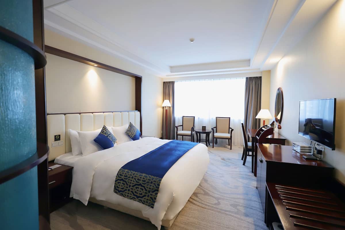Une chambre d’hôtel avec un grand lit, un bureau, une télévision et une vue sur l’extérieur par la fenêtre.