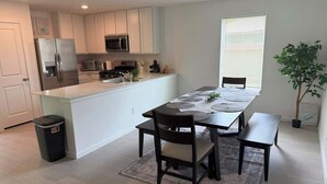 A modern kitchen with white cabinets, a stainless steel refrigerator, and a dining area with a table set for four.