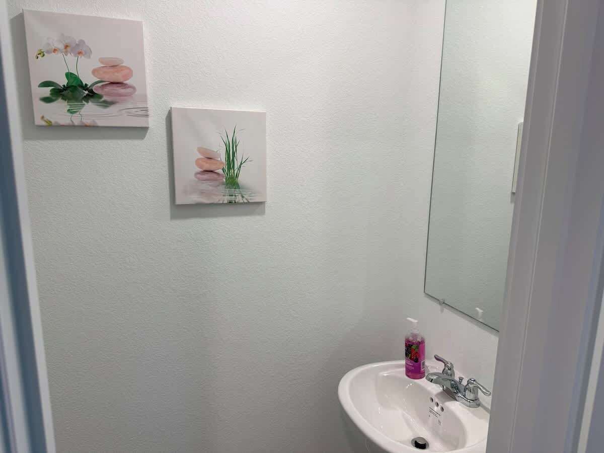 Un bagno con un lavandino bianco, uno specchio e due quadri appesi al muro.