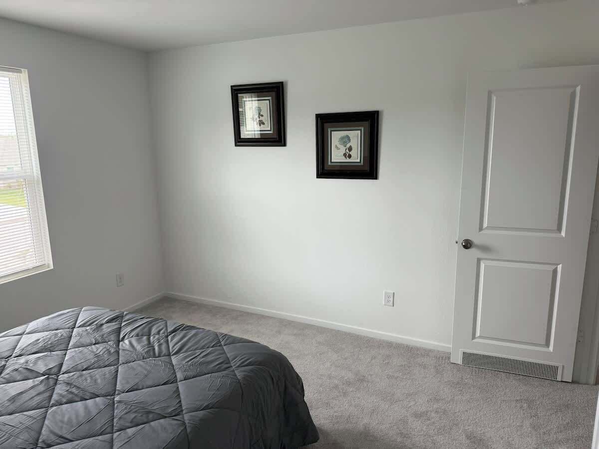 Un dormitorio con una cama, una puerta y dos cuadros en la pared.