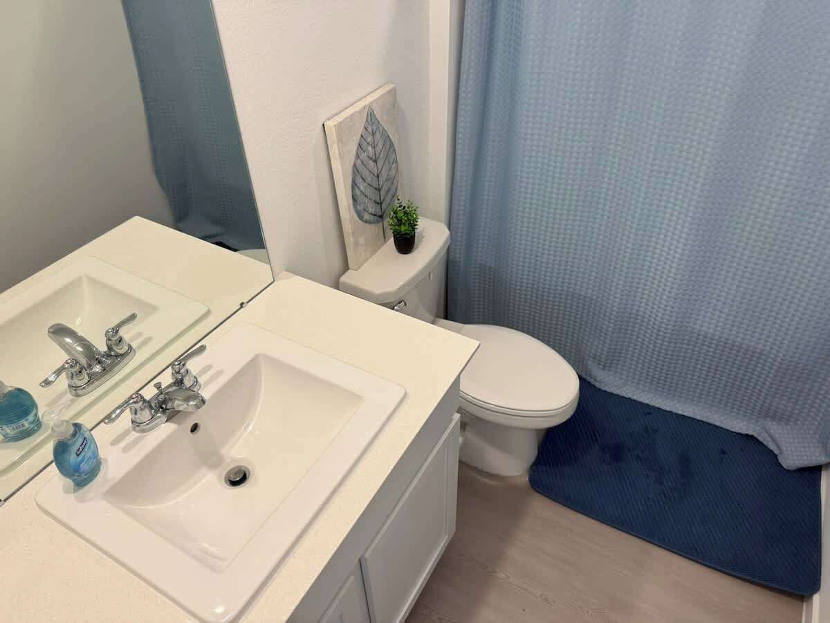 A bathroom with a white sink, two faucets, a mirror, a toilet, and a blue shower curtain.