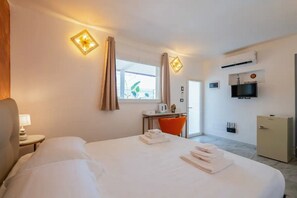 A hotel room with a bed, a desk, a chair, a TV, and a minibar.