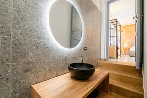 Un baño moderno con un espejo redondo, un lavabo de cerámica negra y un mueble de tocador de madera.