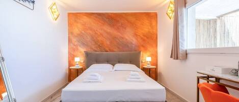 Une chambre d’hôtel avec un grand lit, deux tables de chevet avec des lampes, un bureau avec une chaise et une fenêtre avec des rideaux.