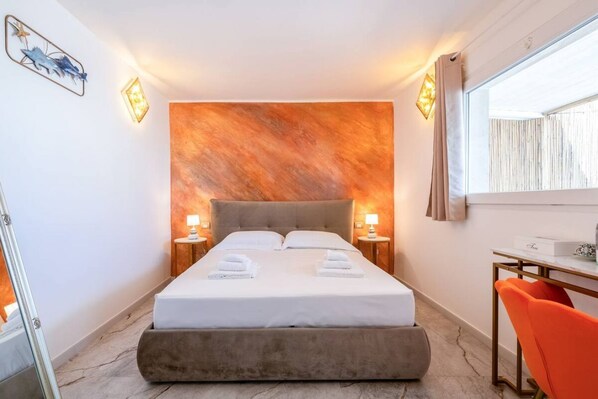 Habitación de hotel con una cama grande, dos mesitas de noche con lámparas, un escritorio con silla y una ventana con cortinas.