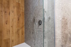 A modern bathroom with a wooden floor, a glass shower enclosure, and a marble wall. - Poema – Where Comfort Meets the Coast (Polignano a Mare)