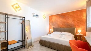 Hotellihuone, jossa on sänky, vaatekaappi, peili, tuoli ja kuvioitu seinä.