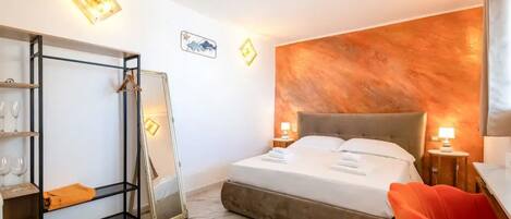 A hotel room with a bed, a wardrobe, a mirror, a chair, and a wall with a textured design.